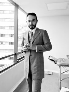 Carlos Bustamante Director médico de aimi en un consultorio en un edificio se cierra el saco del vestido, con corbata, imagen en blanco y negro, aimi medicina integrativa avanzada